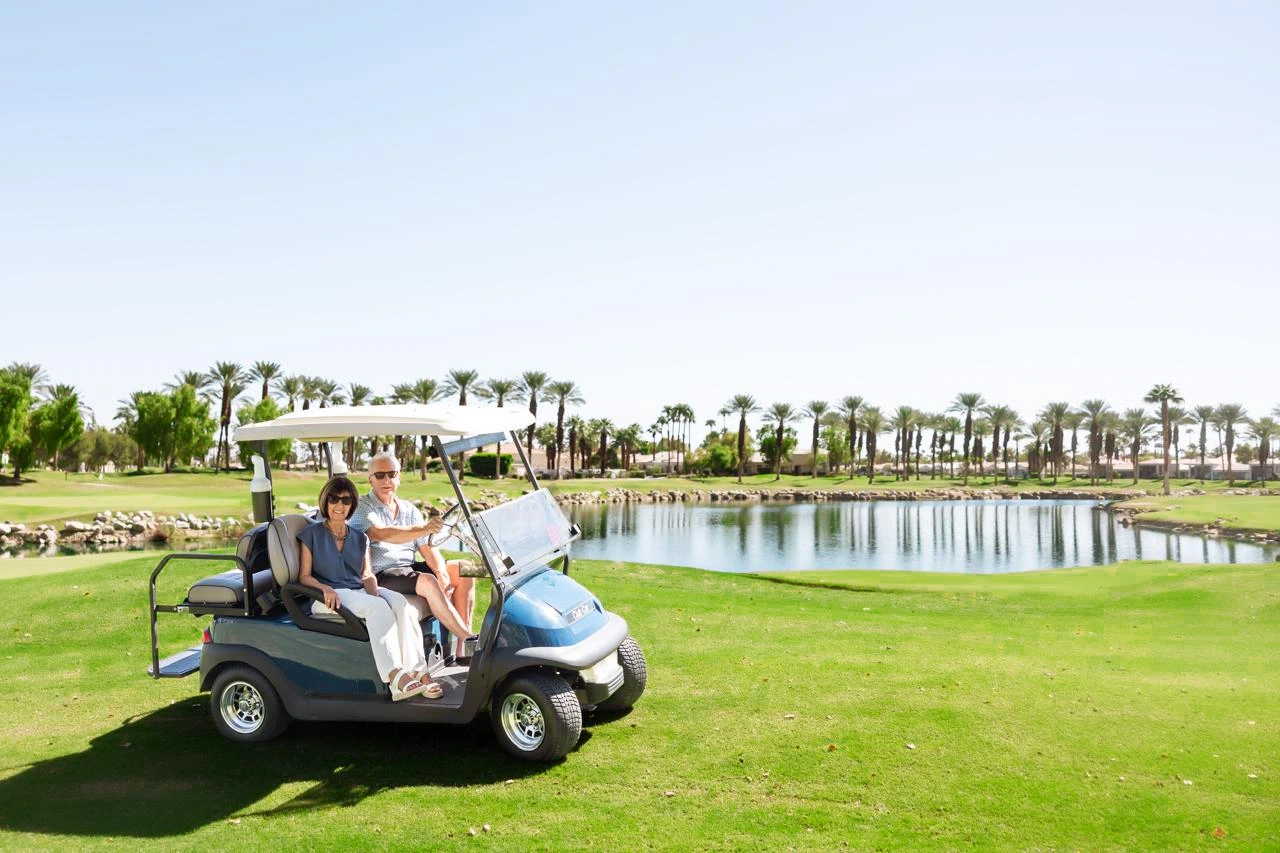 Jim and Cindy Simonson in a golf cart beside a lake lined with palm trees